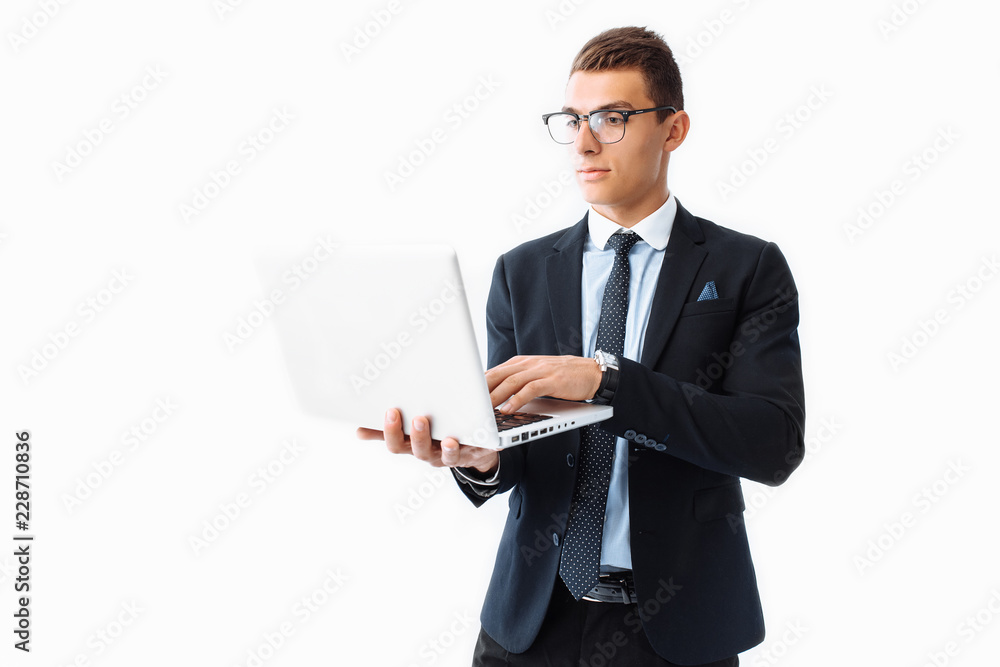 Confident man with glasses, young handsome businessman in a suit holding a laptop and looking at the screen, standing on a white background Confident man with glasses, young handsome businessman in a suit holding a laptop and looking at the screen, standing on a white background