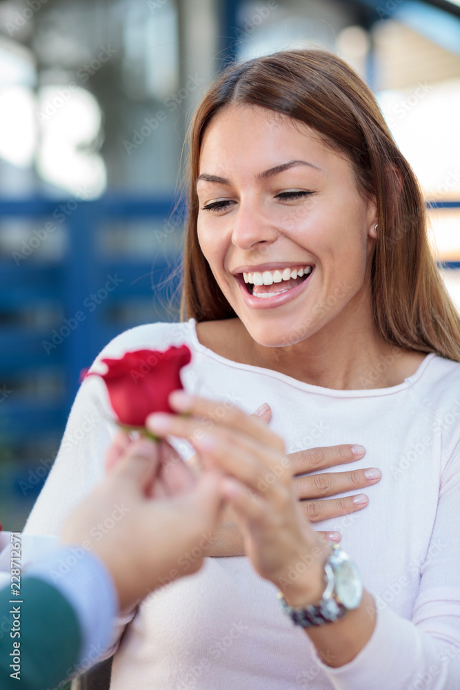 Smiling young woman receiving a single red rose from her boyfriend or husband.