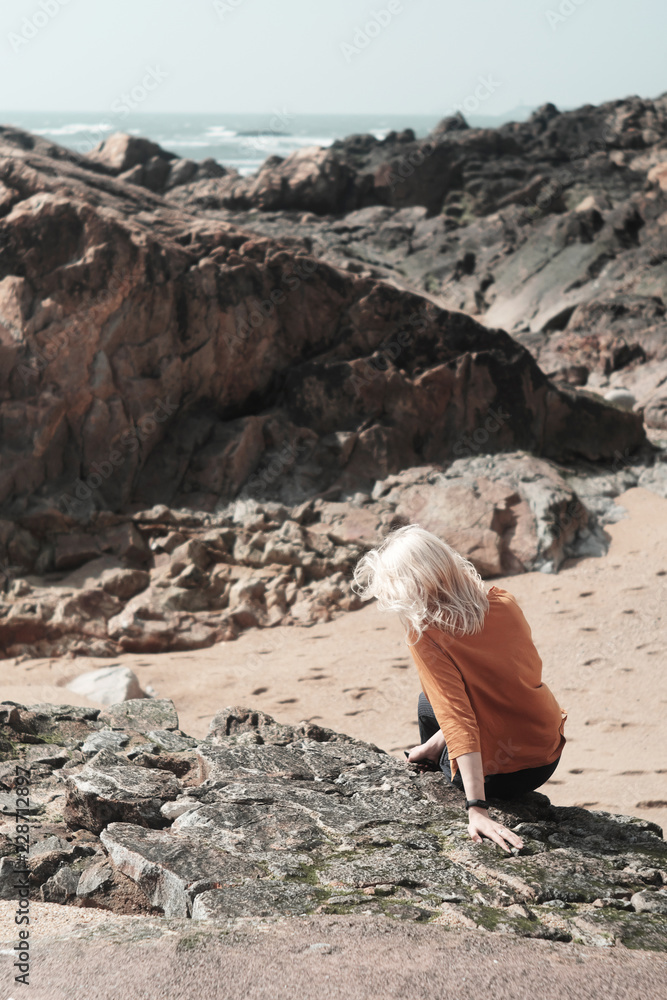 Vertical photo of the girl on the rock is sitting overlooking the rocks by the sea