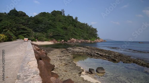 Scenic view of road next to sea shore on tropical island with palm trees as guyman drive past with mini Moke/ beach buggy. Seychelles, Praslin. Slow motion 50p. photo