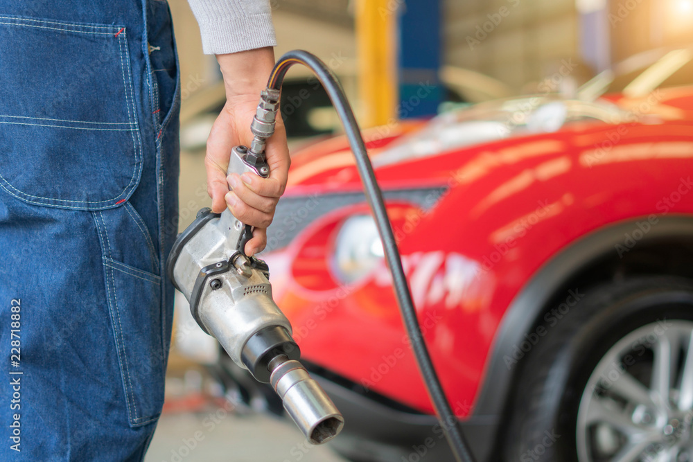 Professional car mechanic working with pneumatic wrench in auto repair service. Repair of wheels Professional car mechanic working with pneumatic wrench in auto repair service. Repair of wheels
