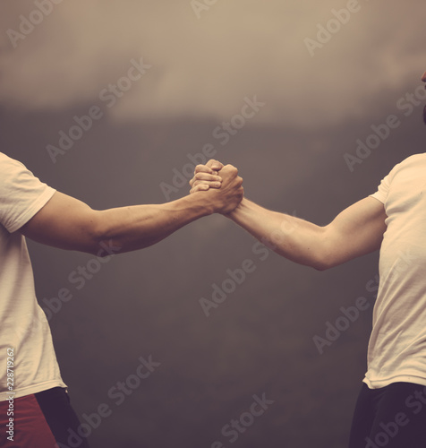 Фотография Two crossfit sports men doing arm wrestling exercise during outdoor workout against cloudy sky background