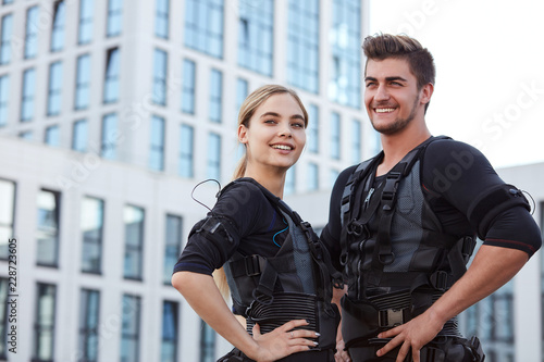 two positive young people wearing ems fitness vest and posing to the camera on the street.copy space photo