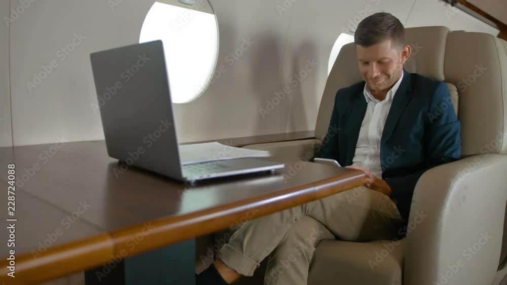 Business man chatting in modern smartphone sitting in comfortable armchair in private jet cabin while plane flighting in the air. Luxury interior apartment look. Middle slider slidetrack shot. Business man chatting in modern smartphone sitting in comfortable armchair in private jet cabin while plane flighting in the air. Luxury interior apartment look. Middle slider slidetrack shot.