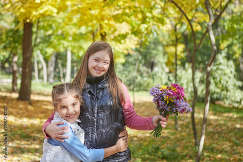 Girl with Down syndrome and little girl in autumn park.