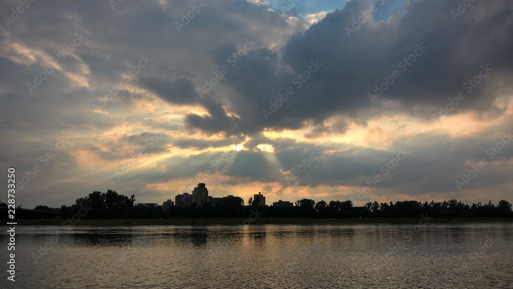 Fototapeta premium Sonnenuntergang am Flussufer mit Sonnenstrahlen im Himmel