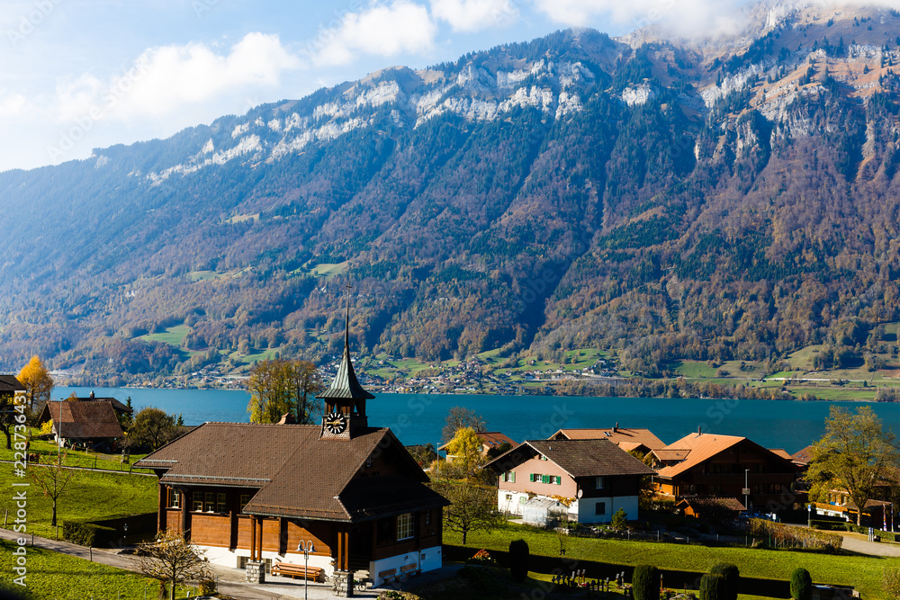 Picturesque alpine meadows, chalets, lake and church with a clocktower in the Swiss Alps