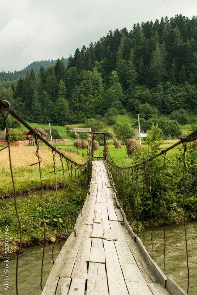 Fototapeta premium Old suspension bridge crossing mountain river. Landscape view