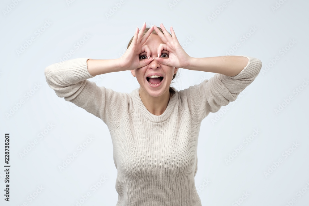 Pretty girl with surprised face holding fingers near eyes like glasses. Mask like super hero or owl Pretty girl with surprised face holding fingers near eyes like glasses. Mask like super hero or owl