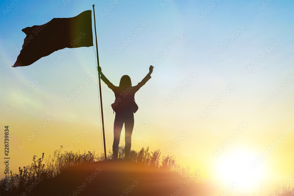 High achievement, silhouettes of the girl, flag of victory on the top of the mountain, hands up. A man on top of a mountain. Conceptual design. Against the dramatic sky with clouds at sunset.