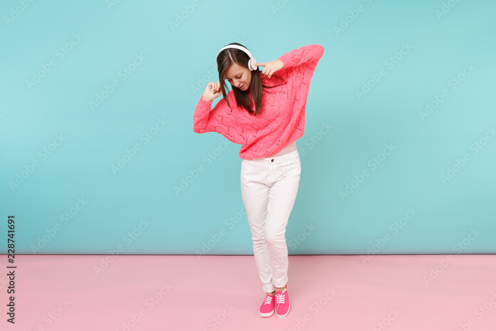 Full length portrait of happy young woman in knitted rose sweater, white pants, headphones isolated on bright pink blue pastel wall background in studio. Fashion lifestyle concept. Mock up copy space. Full length portrait of happy young woman in knitted rose sweater, white pants, headphones isolated on bright pink blue pastel wall background in studio. Fashion lifestyle concept. Mock up copy space.