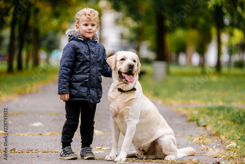 Portrait of cute adorable little Caucasian baby boy sitting with dog in park outside. Smiling child holding animal domestic pet. Happy childhood concept