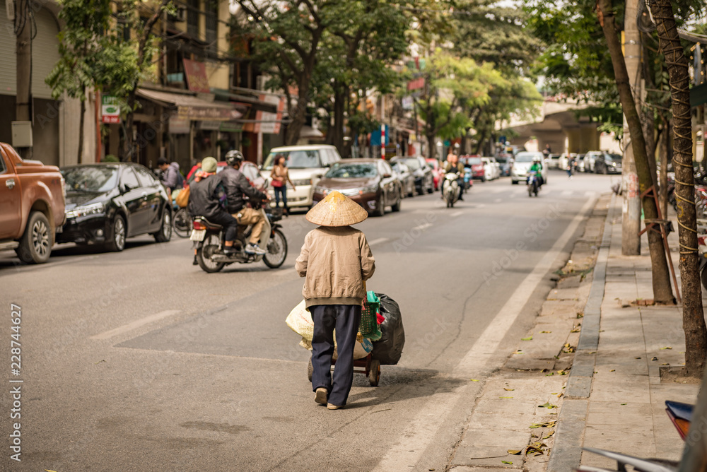 Obraz premium Mit Reishut und Sackkarre auf Hanoi's Straßen unterwegs