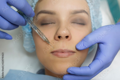 Top view of lips augmentation procedure on a young woman done by a cosmetologist doctor with Hyaluronic acid Injection.