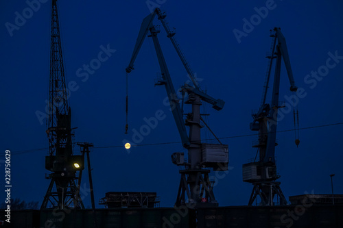 industrial crane lifts moon in blue evening