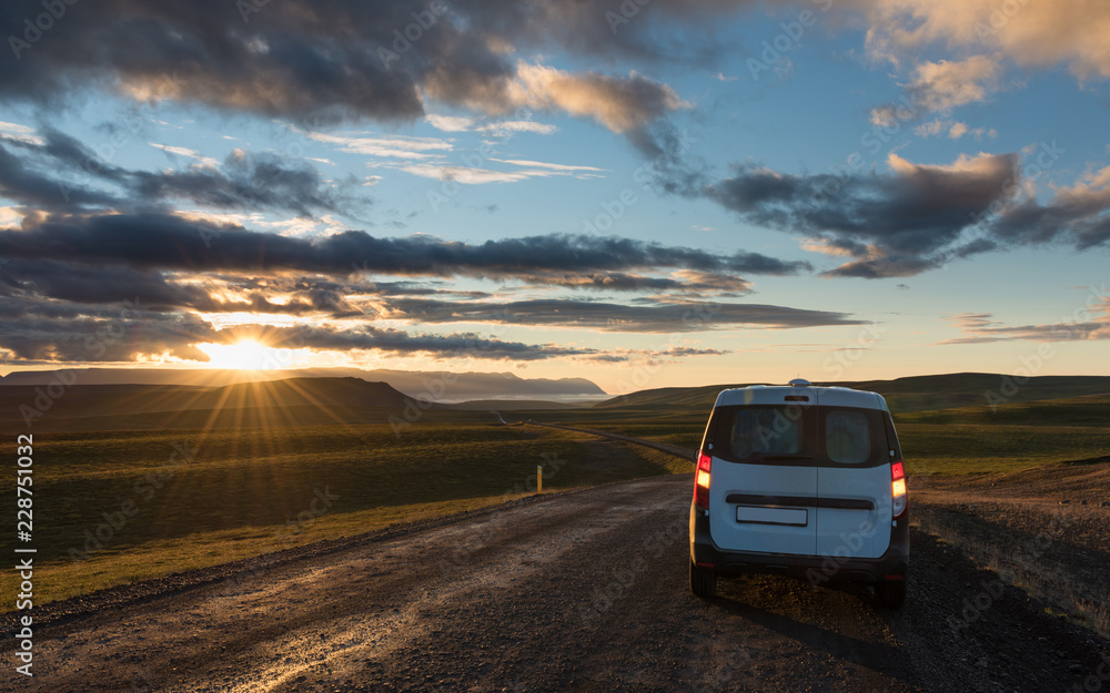 Gravel road along the valley at sunset with lonely car. Car travel in Iceland