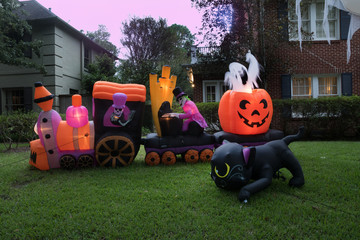 The house is decorated for Halloween: Inflatable train with the dead, big pumpkin, ghost and black cat. Night, Houston, Texas, United States