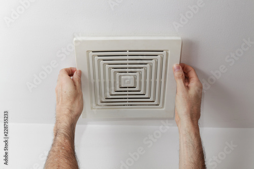 Man's hands removing air duct cover from ceiling