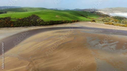 Bay during low tide surrounded by green hills, waves and beach are visible on the other side of the hill photo