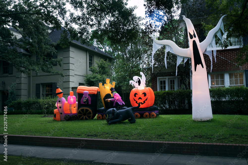 Fototapeta premium The house is decorated for Halloween: Inflatable train with the dead, big pumpkin, black cat huge and small ghost. Night, Houston, Texas, United States