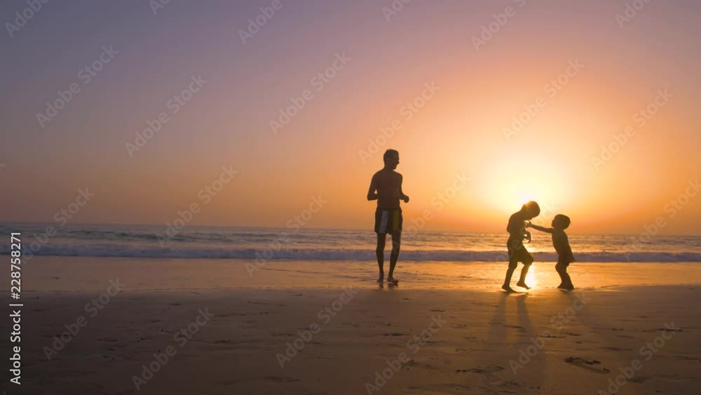 Silhouette of father with two children in the beach at sunset Silhouette of father with two children in the beach at sunset