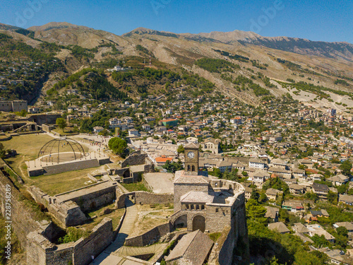 Drone view of Gjirokastër Castle and city surrounded by mountains and blue sky. Also known as Kalaja, the fortress is a UNESCO heritage site in Albania