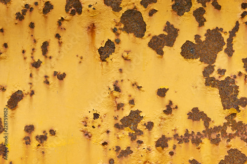 Close-up of weathered yellow painted metal surface with large and small rusty spots