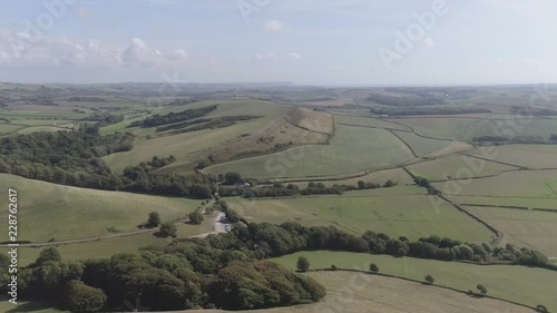 Wide aerial shot tracking across the fields surrounded by Chesil Beach and the Village of Abbotsbury, Dorset. Cropped photo