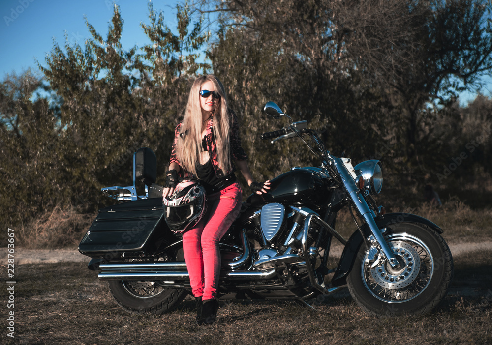 Biker blond woman outdoor with her motorcycle.
