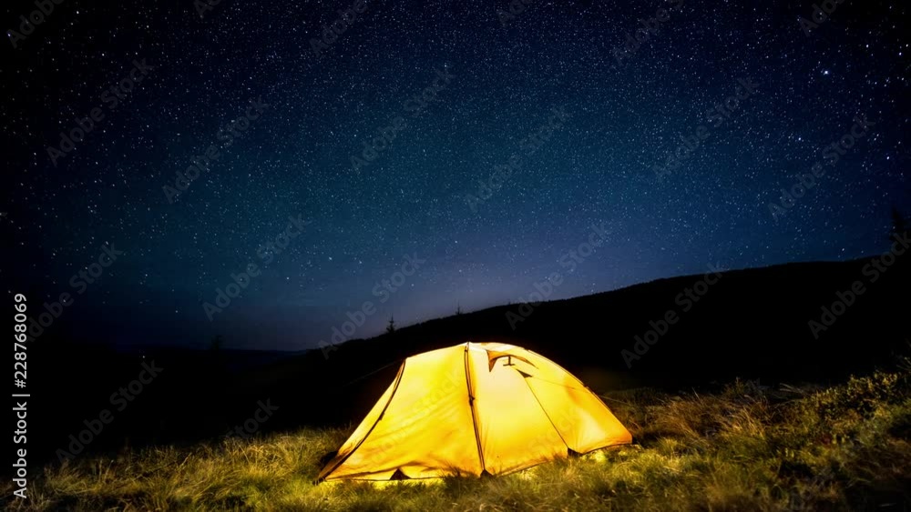 Time-lapse. Glowing camping tent in the night mountain forest under a starry sky Time-lapse. Glowing camping tent in the night mountain forest under a starry sky