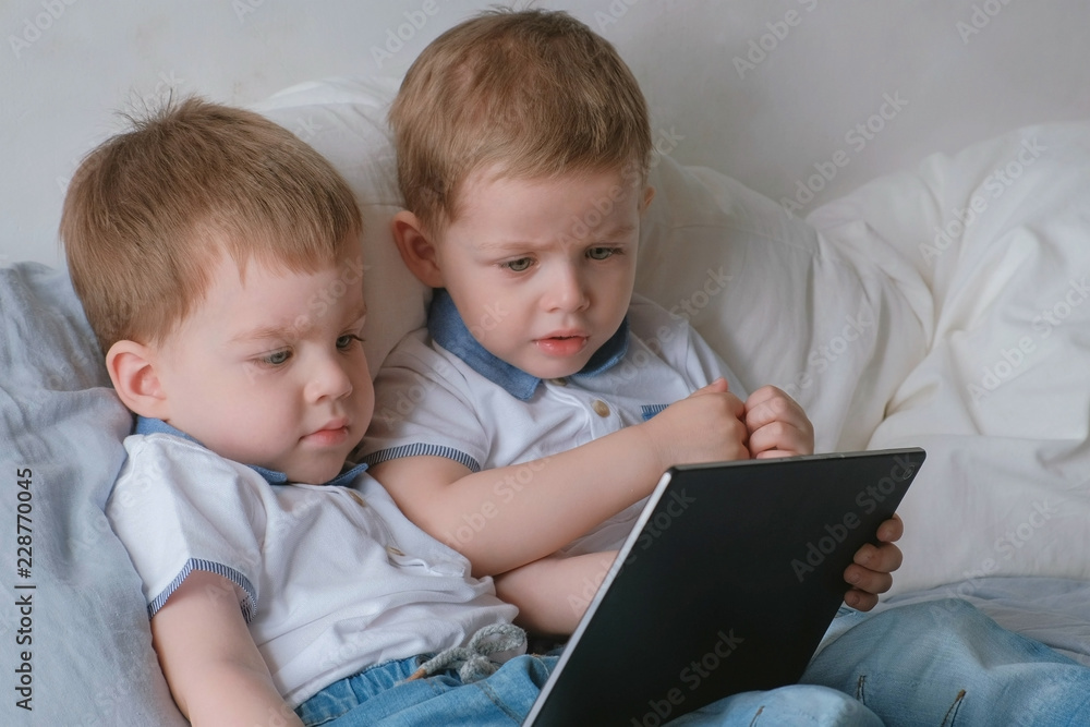 Kids with tablet. Two boys twins toddlers looking cartoon at tablet lying on the bed. Kids with tablet. Two boys twins toddlers looking cartoon at tablet lying on the bed.
