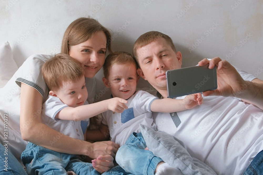 Dad makes family selfie on mobile phone. Mom, dad and two brother twins toddlers. Dad makes family selfie on mobile phone. Mom, dad and two brother twins toddlers.