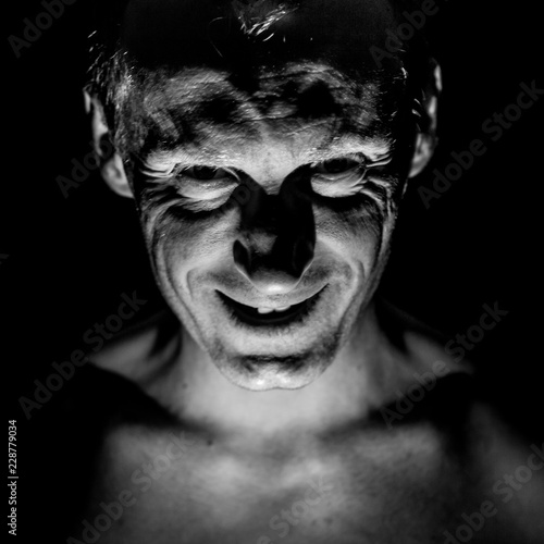 Stylish portrait of adult caucasian man. He smiles like maniac and seems like maniac or crazy. Black and white shot, low-key lighting.