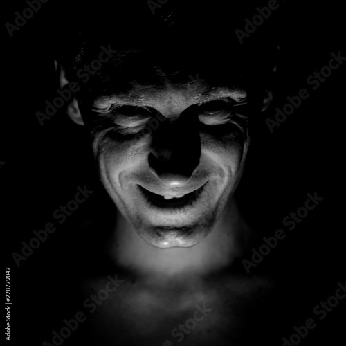 Stylish portrait of adult caucasian man. He smiles like maniac and seems like maniac or crazy. Black and white shot, low-key lighting.