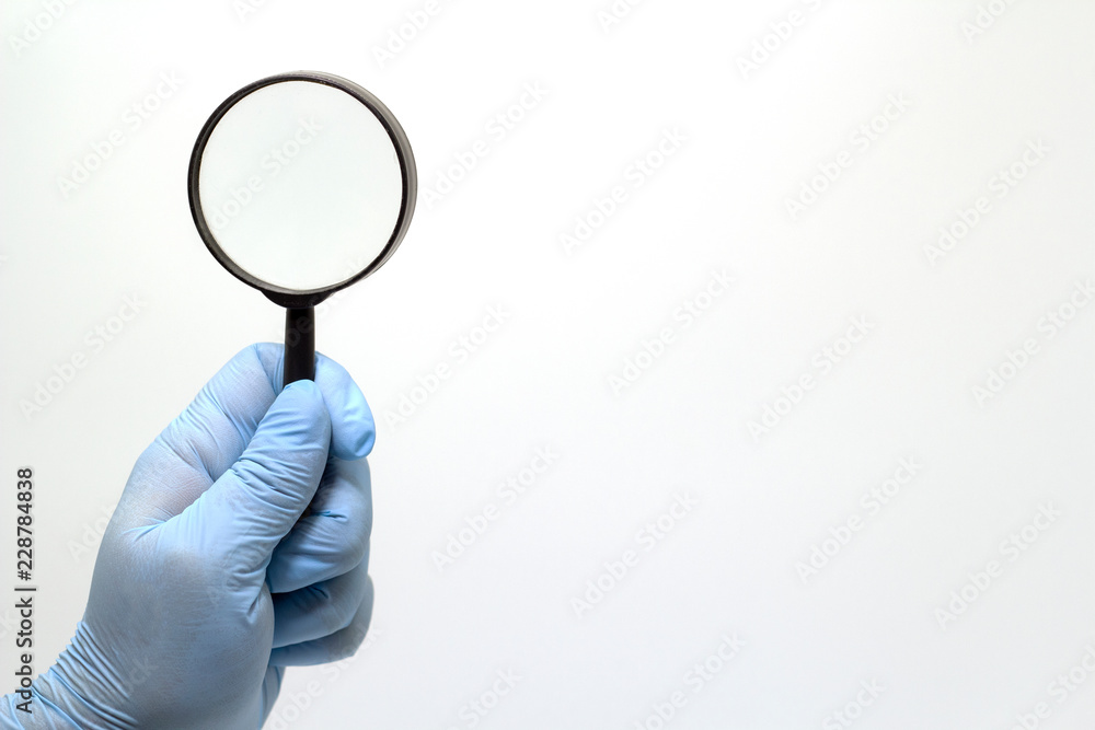 Surgeon's hand in a blue medical glove holding a magnifying glass . The concept of health. Surgeon's hand in a blue medical glove holding a magnifying glass . The concept of health.