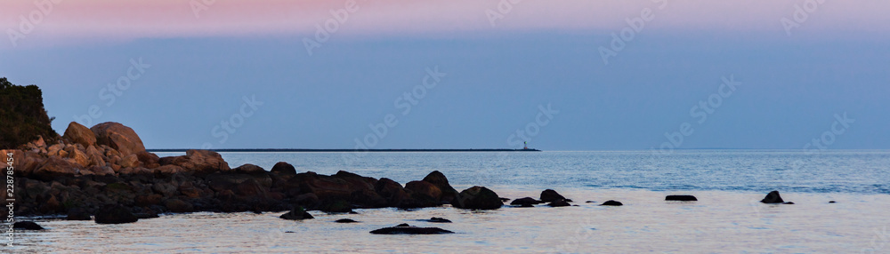 Panorama of coastline with peninsula and green beacon lighting at dusk