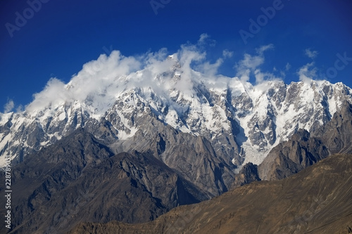 Snow capped Ultar Sar mountain peak behind the clouds. Batura Muztagh, Karakoram range. Hunza valley, Gilgit Baltistan Pakistan.