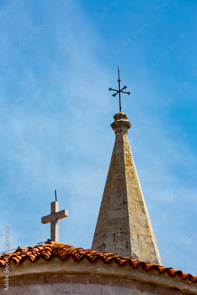 Beautiful medieval architecture, close-up detailed view of the sharp and mighty church needle of St.John with cardinal arrows in Budva,Montenegro. Spring daytime cityscape with blurred cross in front Beautiful medieval architecture, close-up detailed view of the sharp and mighty church needle of St.John with cardinal arrows in Budva,Montenegro. Spring daytime cityscape with blurred cross in front