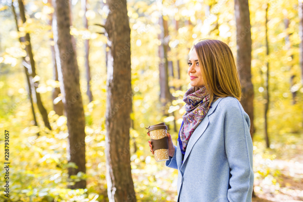 Autumn, nature and people concept - Young beautiful woman in blue coat holding a cup of coffee Autumn, nature and people concept - Young beautiful woman in blue coat holding a cup of coffee