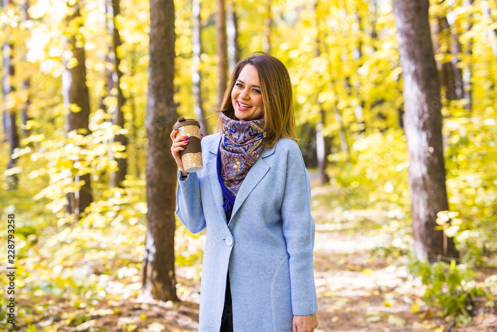 Autumn, nature and people concept - Young beautiful woman in blue coat holding a cup of coffee Autumn, nature and people concept - Young beautiful woman in blue coat holding a cup of coffee