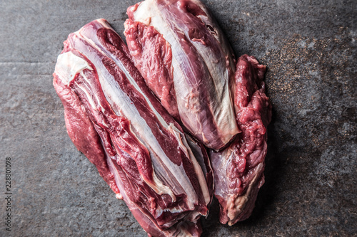 Portion of raw beef shank on dark butcher board