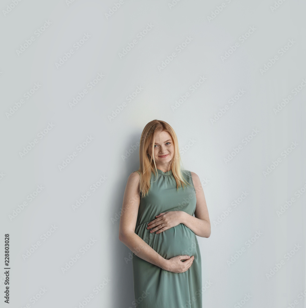 Obraz premium Young pregnant woman touching belly on light background