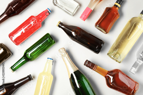 Bottles with different alcoholic drinks on light background, flat lay