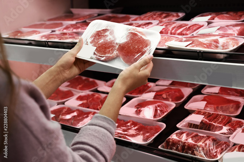 Woman taking packed pork meat from shelf in supermarket