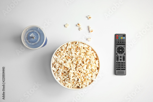 Bucket with popcorn, cup of beverage and TV remote on white background, top view. Watching cinema