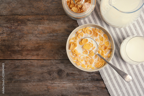 Flat lay composition with healthy cornflakes and milk in bowl on wooden table. Space for text