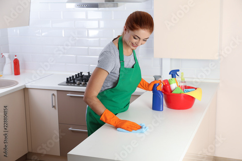Woman in protective gloves cleaning kitchen table with rag, indoors