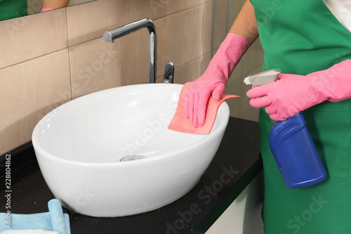 Fototapeta Naklejka Na Ścianę i Meble -  Woman in protective gloves cleaning bathroom sink with rag