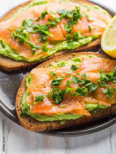 Rye bread avocado toasts with smoked salmon on white wooden board