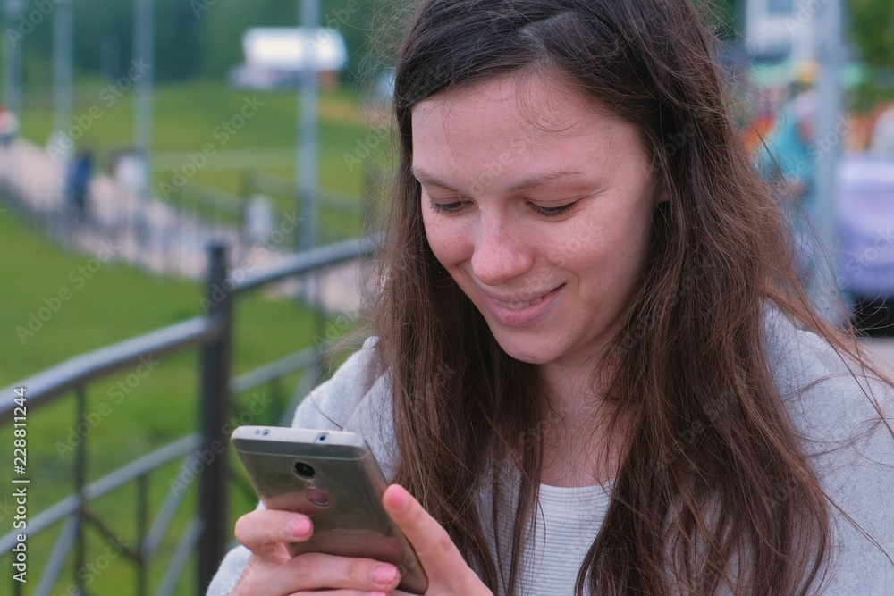 Young brunette woman chatting, typing a message on mobile phone walking along the promenade in the city. Young brunette woman chatting, typing a message on mobile phone walking along the promenade in the city.